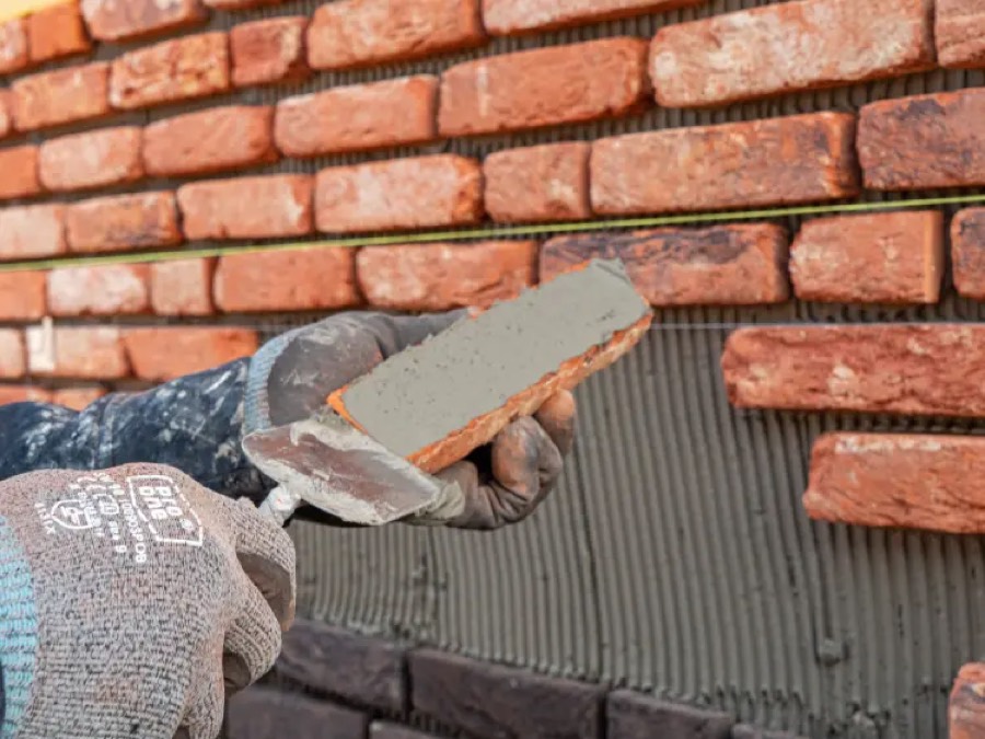 Vakman met werkhandschoenen brengt lijm aan op een rode steenstrip voor een getande lijmlaag