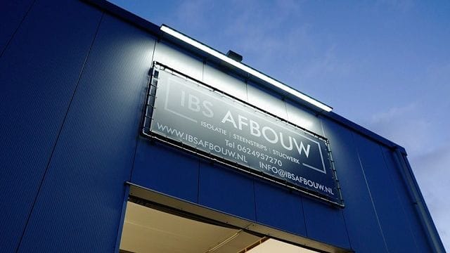 Bedrijfshal met het logo van IBS Afbouw op de gevel, bij avondlicht