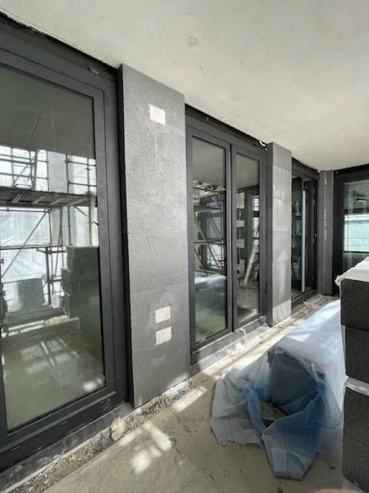 Binnenzijde van het gebouw met grote glaspartijen en donkere kozijnen tijdens de bouw van De Hoogh Amsterdam