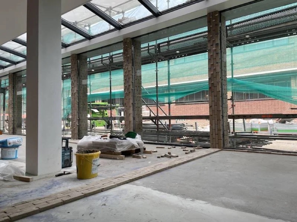 Overzicht van de glazen hal met betonnen kolommen en een steenstripswand tijdens de bouw van het gemeentehuis van Katwijk