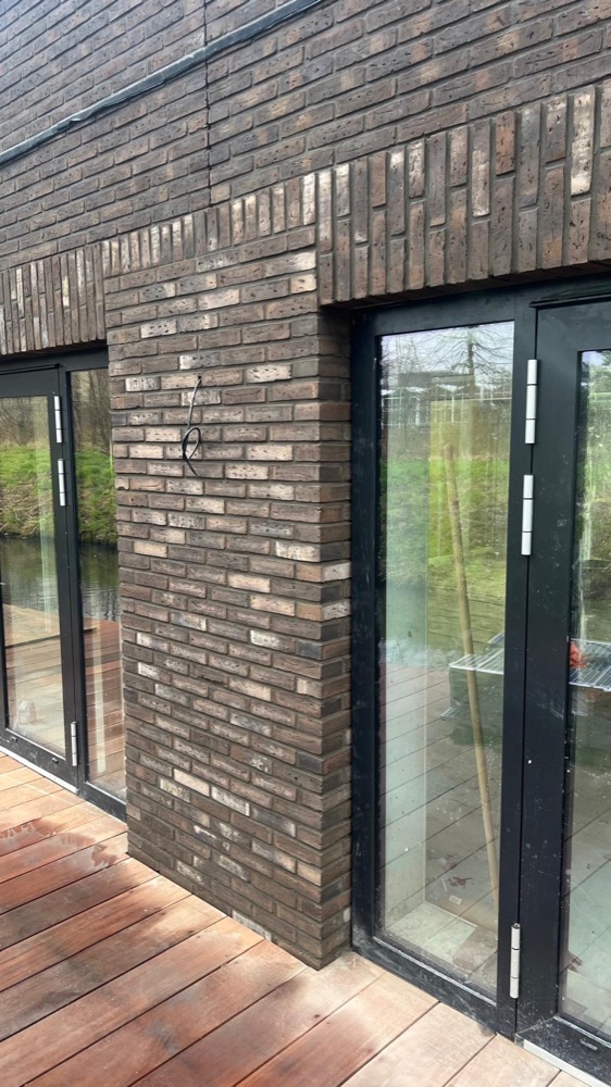 Keramische steenstrips naast een glazen pui met donker kozijn, boven een houten terras