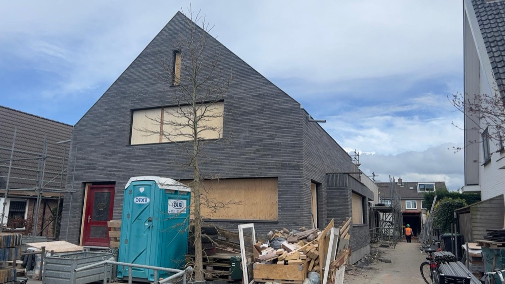 Puntgevel bekleed met grijze steenstrips bij de voormalige bakkerij in Heiloo, met bouwmaterialen op het erf