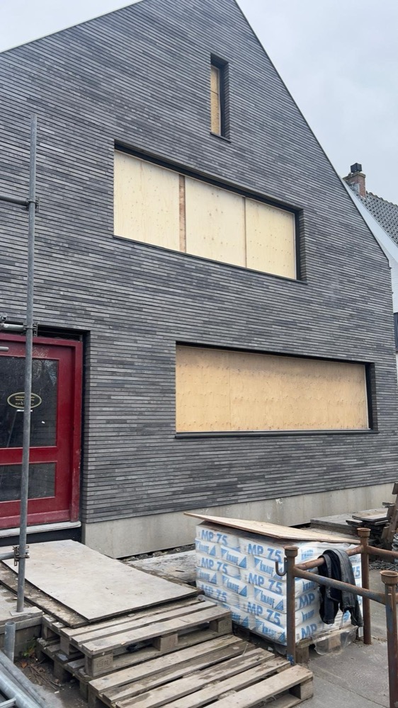 Zijgevel met grijze steenstrips en een rode deur bij de transformatie in Heiloo
