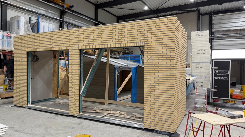 Brede prefab module met gele minerale steenstrips en openingen voor kozijnen