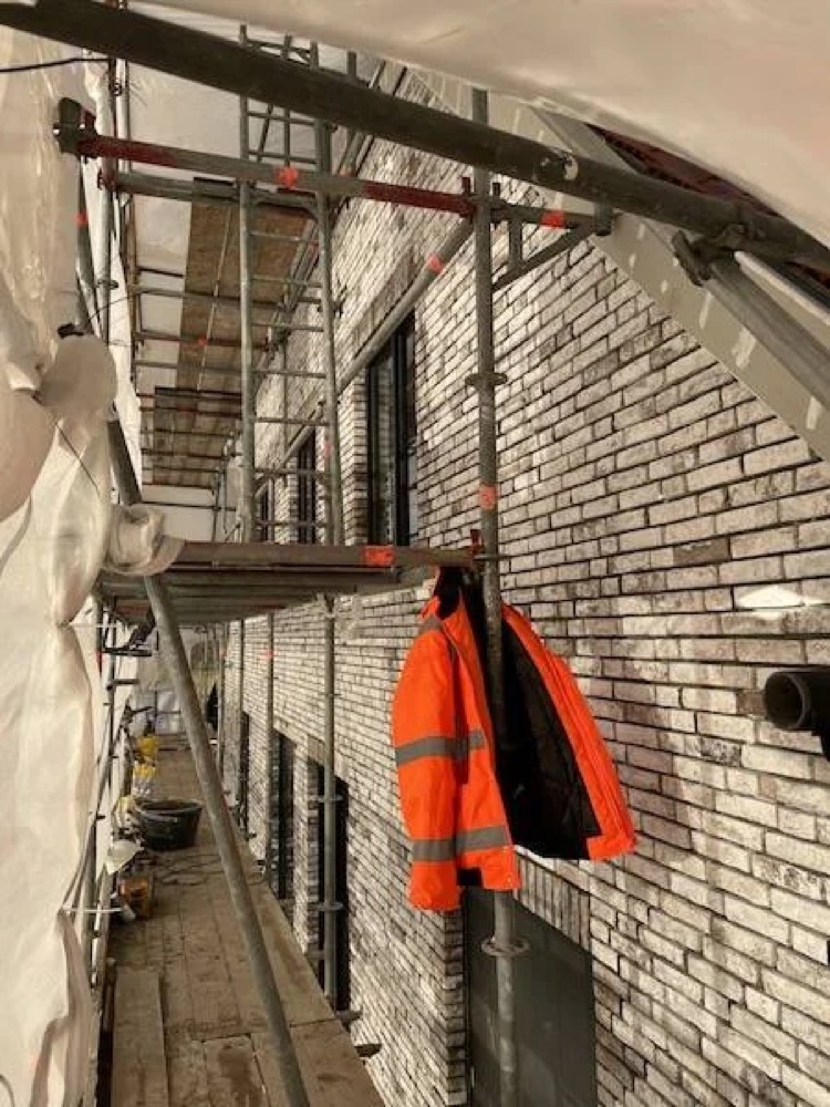 Vakman in werkkleding op een steiger tegen een gevel met steenstrips in Alkmaar