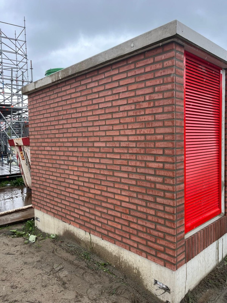 Trafostation met rode steenstrips en rode ventilatiedeuren op een bouwterrein