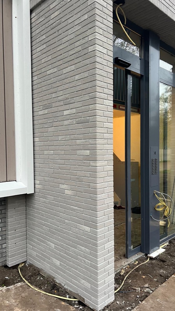 Hoek van een traphuis-omlijsting met lichtgrijze minerale steenstrips naast een glazen pui