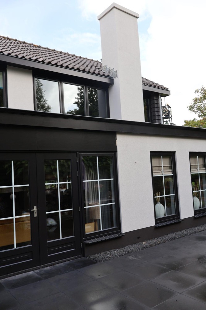 Achtergevel van de villa in Koedijk met witte schoorsteen, glazen deuren en donkere houten gevelbekleding