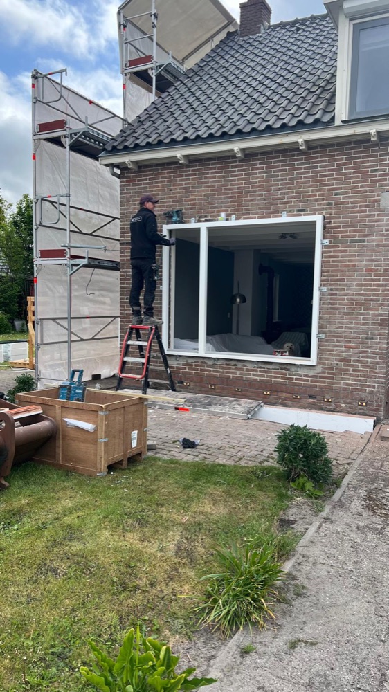 Vakman plaatst een nieuw kozijn met triple glas in de voorgevel, naast een steiger