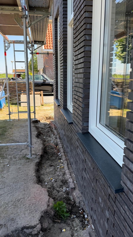 Wit kozijn in de donkere steenstripsgevel met een natuurstenen dorpel, naast de steiger
