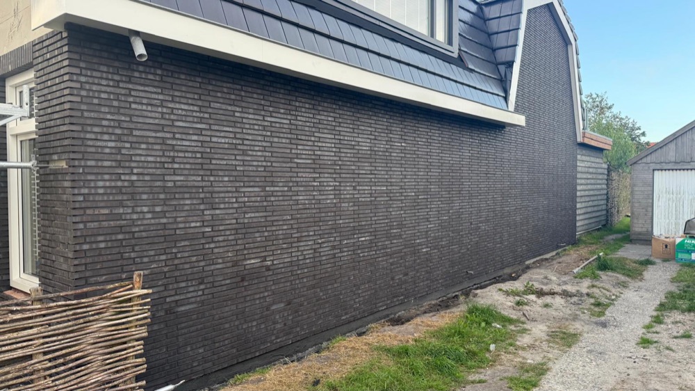 Lange zijgevel van de woning in Julianadorp met donkere steenstrips onder de dakrand