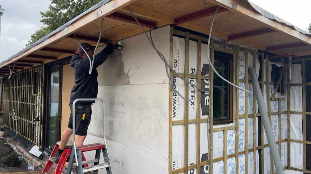 Vakman op een ladder bij de dakrand met houten regelwerk en folie vóór de plaatsing van de gevelbekleding