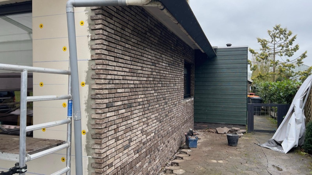 Isolatieplaten met gele pluggen naast afgewerkte steenstrips bij een woonhuis in Andijk