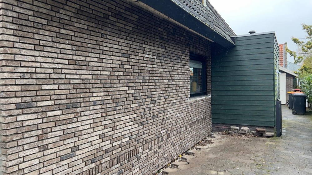 Gevel met gemêleerd bruine steenstrips en een donkergroen zijvlak bij het woonhuis in Andijk
