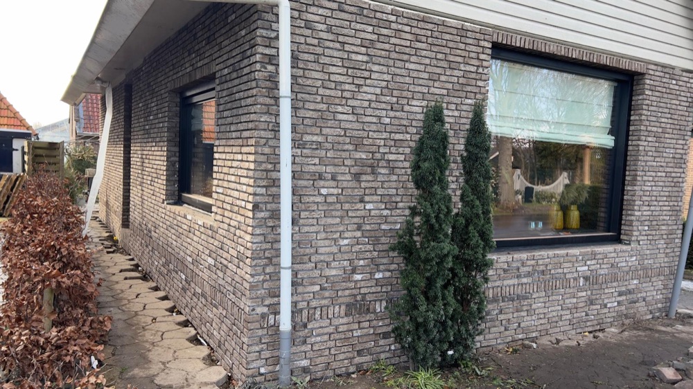 Zijgevel van het woonhuis in Andijk met gemêleerd bruine steenstrips, donkere kozijnen en een hemelwaterafvoer