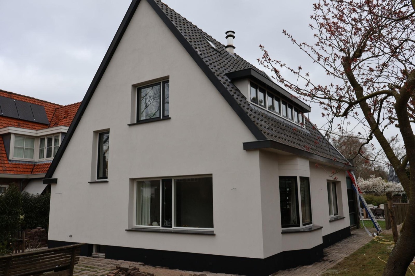 Woonhuis met puntgevel in Bergen na de gevelisolatie, met een witte sierpleistergevel en een donkere plint
