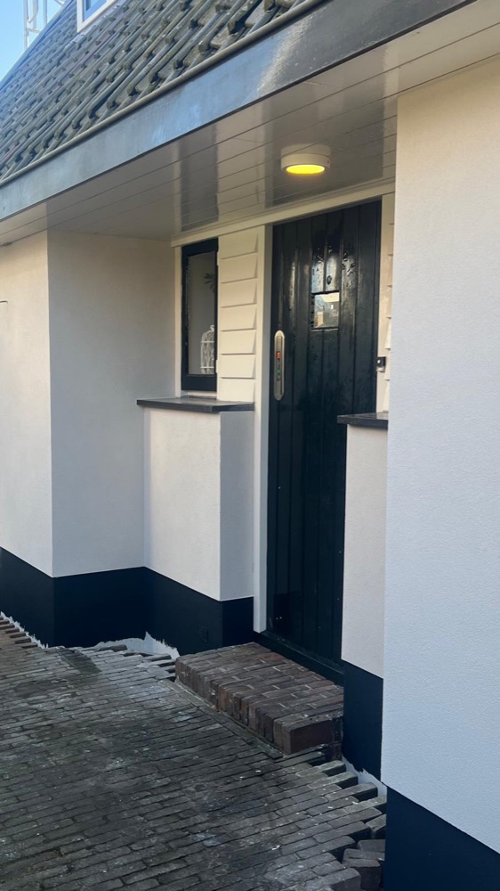 Entree van het woonhuis in Bergen met witte sierpleister en een donkere plint langs het pad