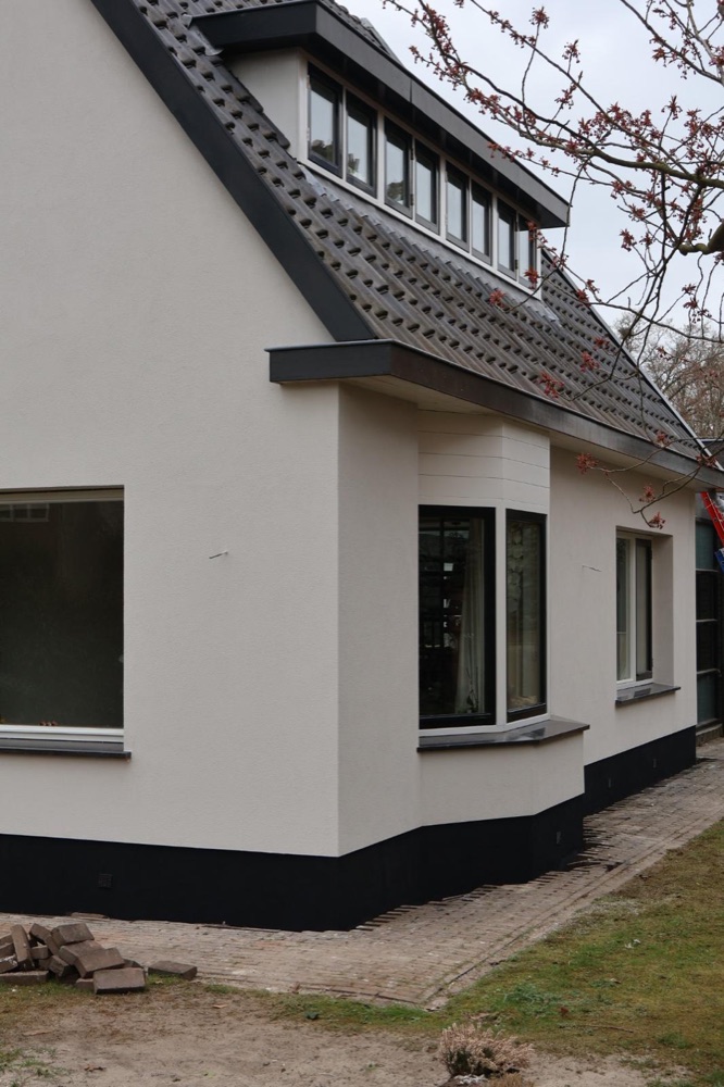 Erker en dakkapel van het woonhuis in Bergen na de gevelisolatie, met witte sierpleister en donkere plint