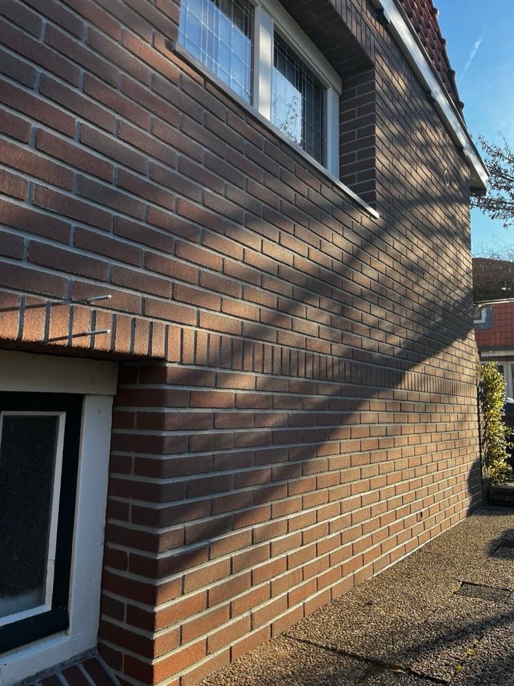 Gevelhoek met donkere minerale steenstrips en een wit kozijn in Bussum