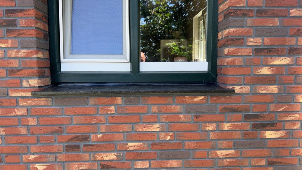 Close-up van rode minerale steenstrips met donkere voegen rond een donkergroen kozijn in Callantsoog