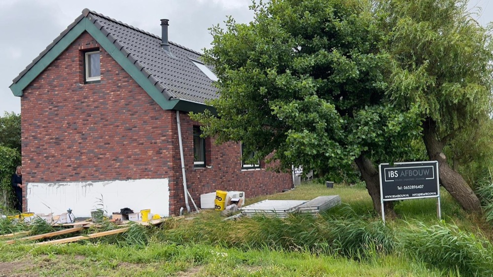 Gevel in Callantsoog halverwege bekleed met rode minerale steenstrips, onder steigers