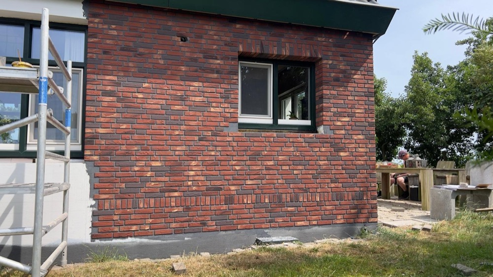 Gevelhoek met rode minerale steenstrips en een steiger naast nog witte gevelvlakken in Callantsoog