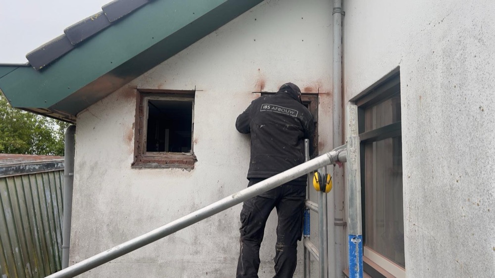 Vakman aan het werk op de oorspronkelijke witte gevel van het woonhuis in Callantsoog