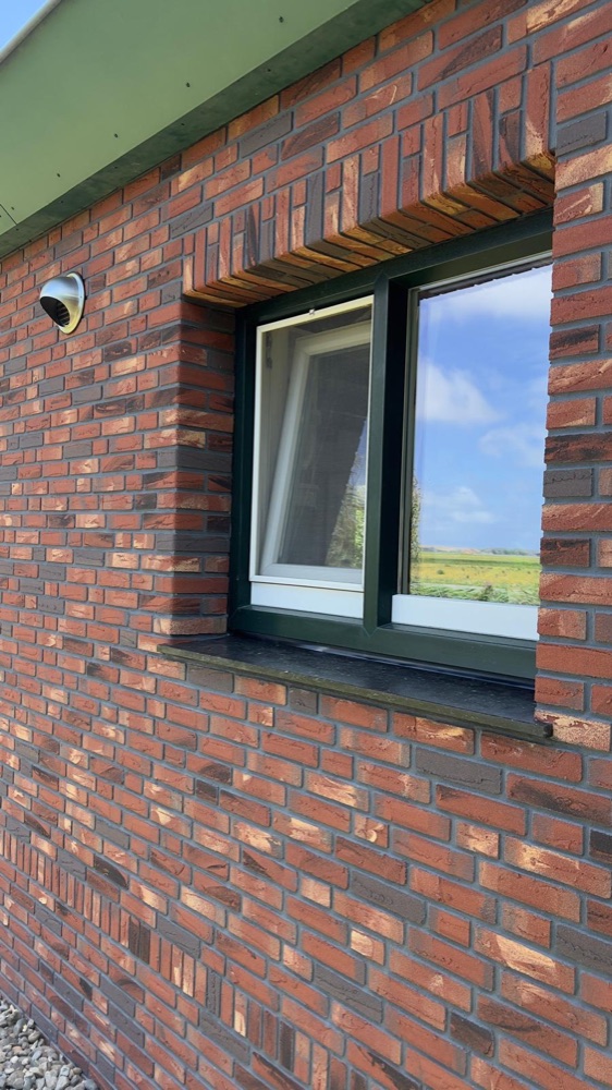 Raam in een gevel van rode minerale steenstrips in Callantsoog, met strips in de dagkant