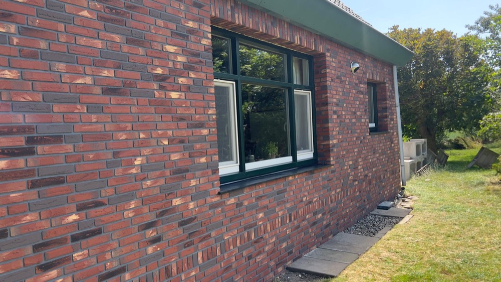 Langsgevel van een woonhuis in Callantsoog met rode minerale steenstrips en donkergroene kozijnen