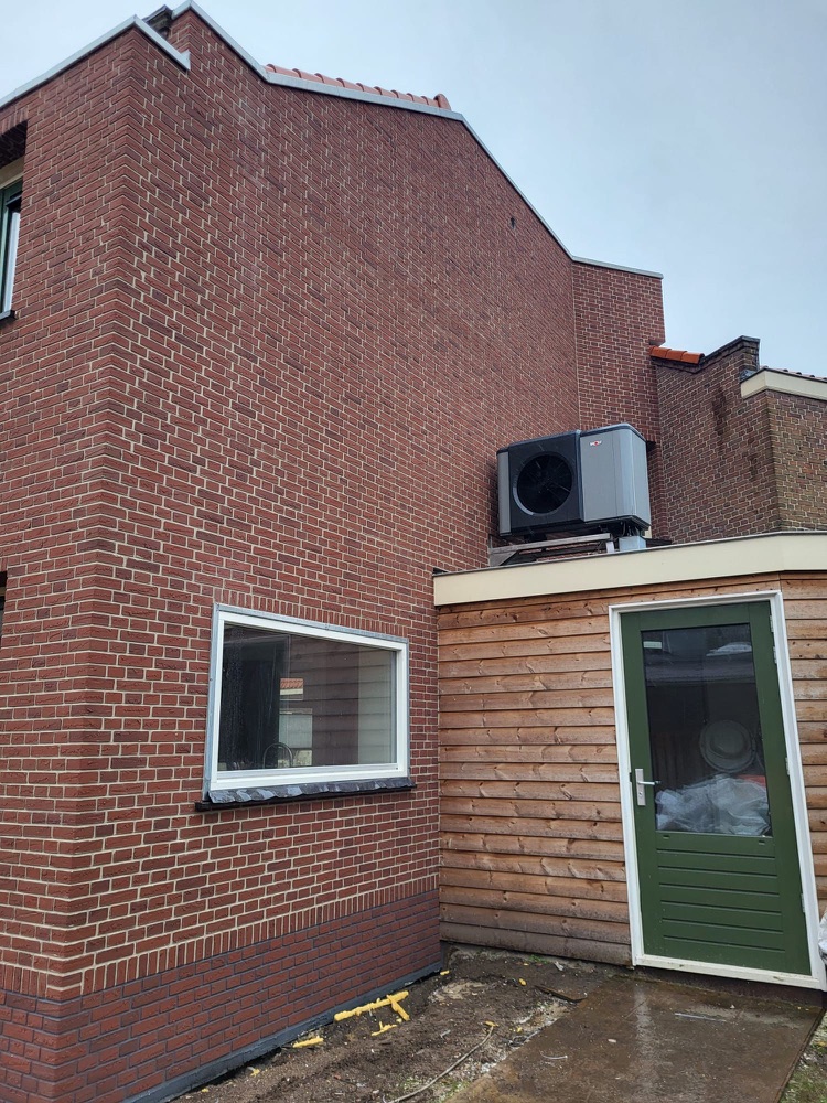 Andere zijde van het woonhuis in Haarlem met rode minerale steenstrips, een buitenunit en een groene deur