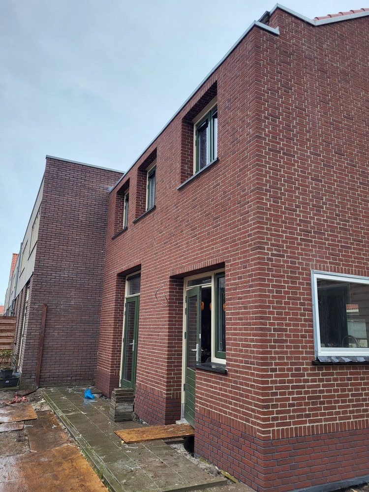 Gevelhoek van het woonhuis in Haarlem met rode minerale steenstrips en groene kozijnen