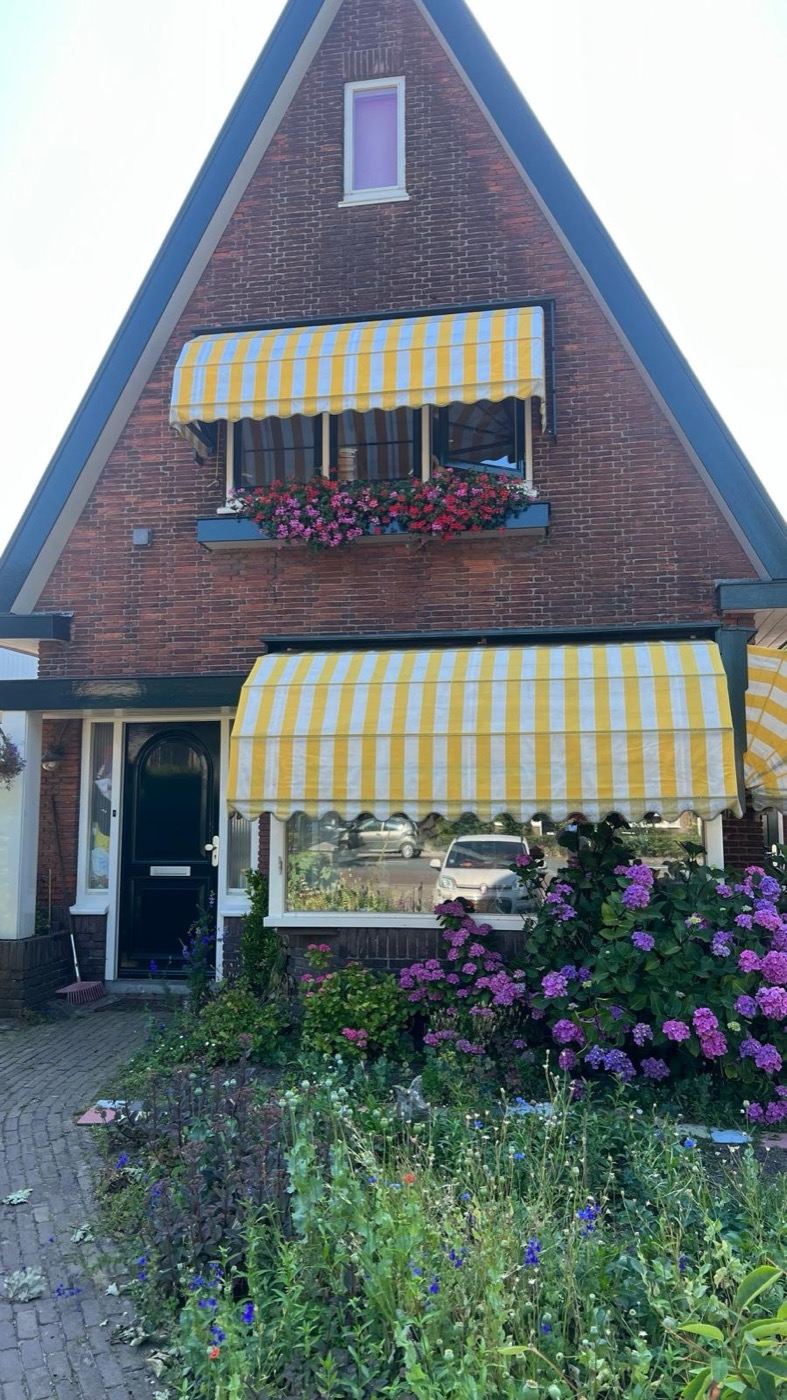 Voorgevel van het woonhuis in Heiloo vóór de renovatie, met donkere baksteen, een bloembak en gele zonneschermen