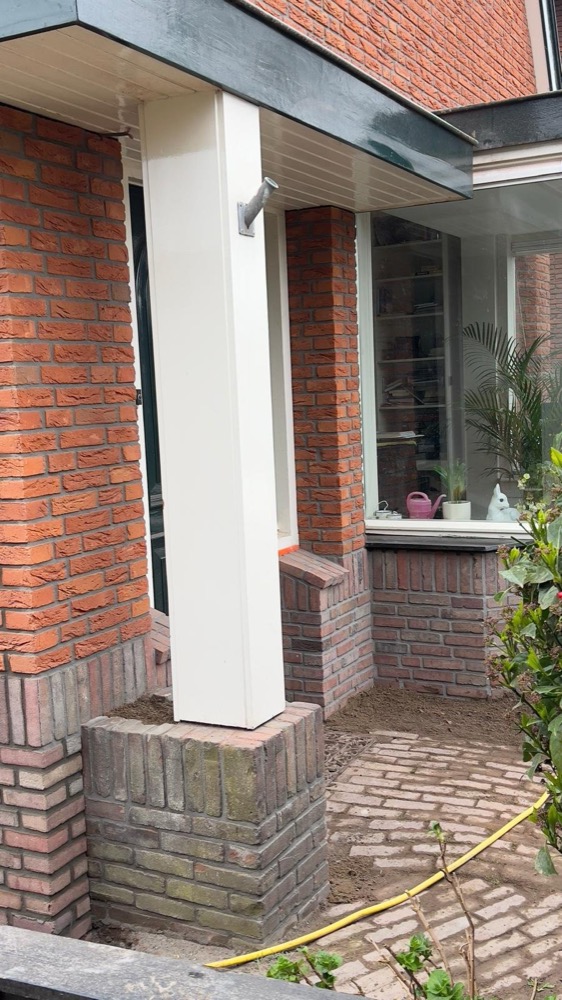 Entree met witte zuil en baksteenwand bij het woonhuis in Heiloo