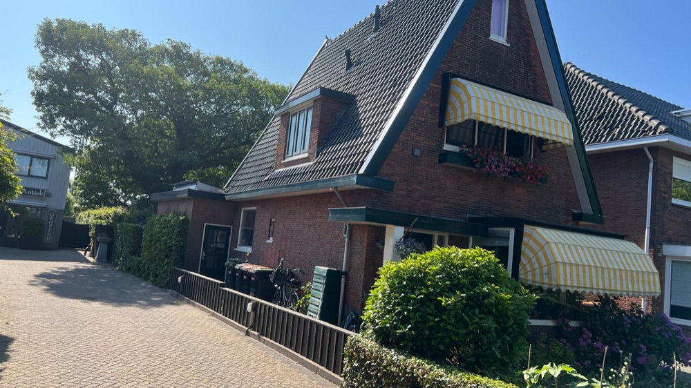 Het woonhuis in Heiloo vóór de renovatie, gezien vanaf de oprit, met donkere baksteengevel en gele zonneschermen
