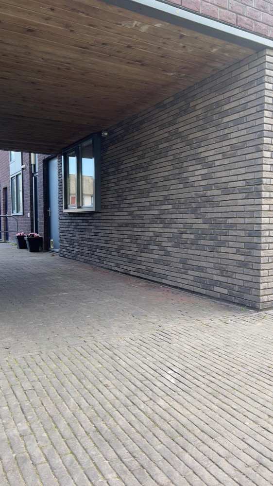 Overdekte doorgang met een houten plafond en een wand van donkere steenstrips