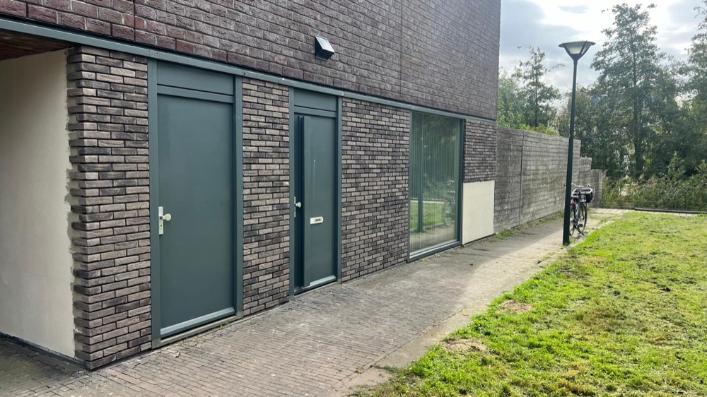 Gevel van het woonhuis in Hoofddorp met gezaagde steenstrips, twee deuren en een raam naast een grasstrook