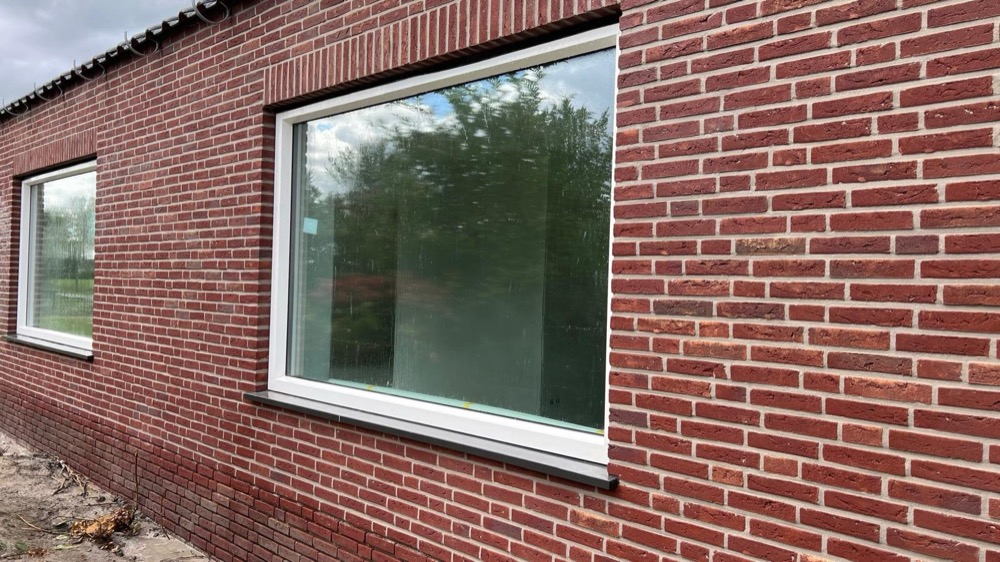 Groot wit kozijn in een gevel van donkerrode steenstrips met lichte voegen in Langedijk