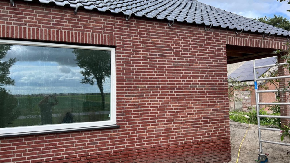 Hoek van de aanbouw in Langedijk met donkerrode steenstrips, een groot raam en een open doorgang