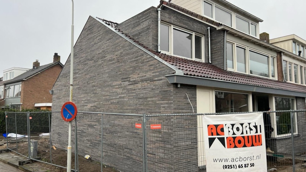 Kopgevel van gemêleerd grijze steenstrips naast een gesloten voorgevel in Limmen
