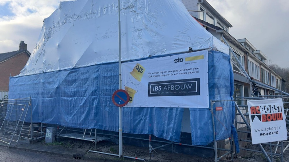 Woning in Limmen volledig ingepakt in blauw zeil tijdens de uitvoering, met een banner van IBS Afbouw